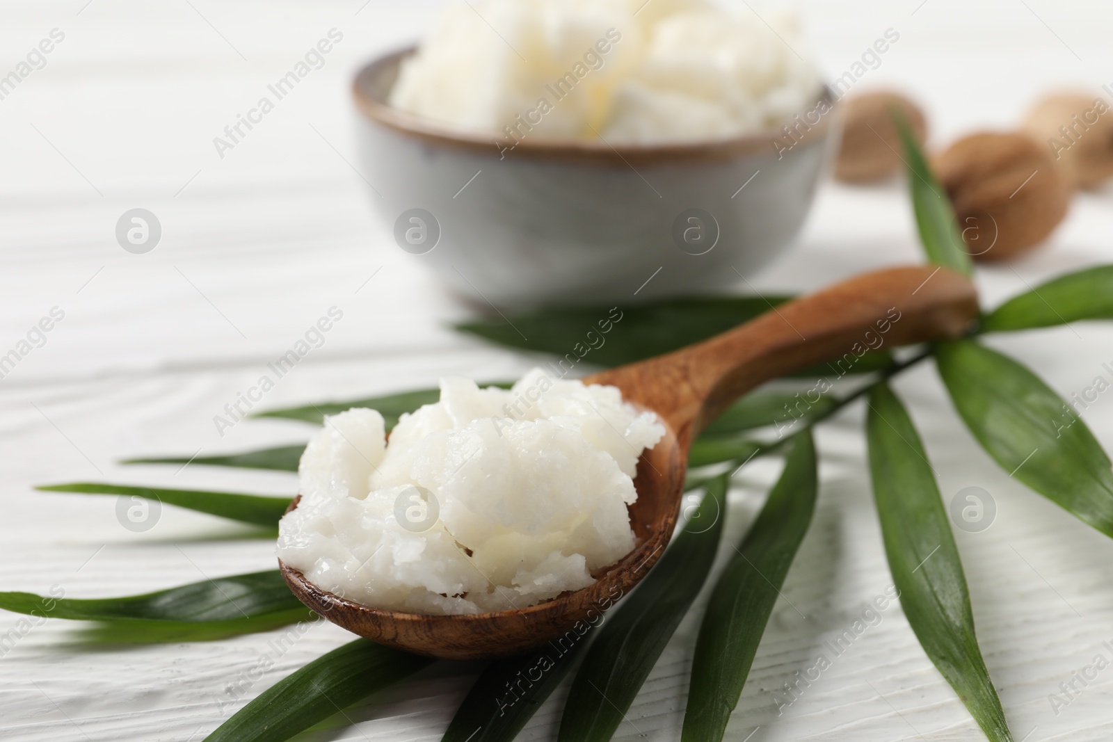 Photo of Shea butter in spoon and nuts on white wooden table, closeup