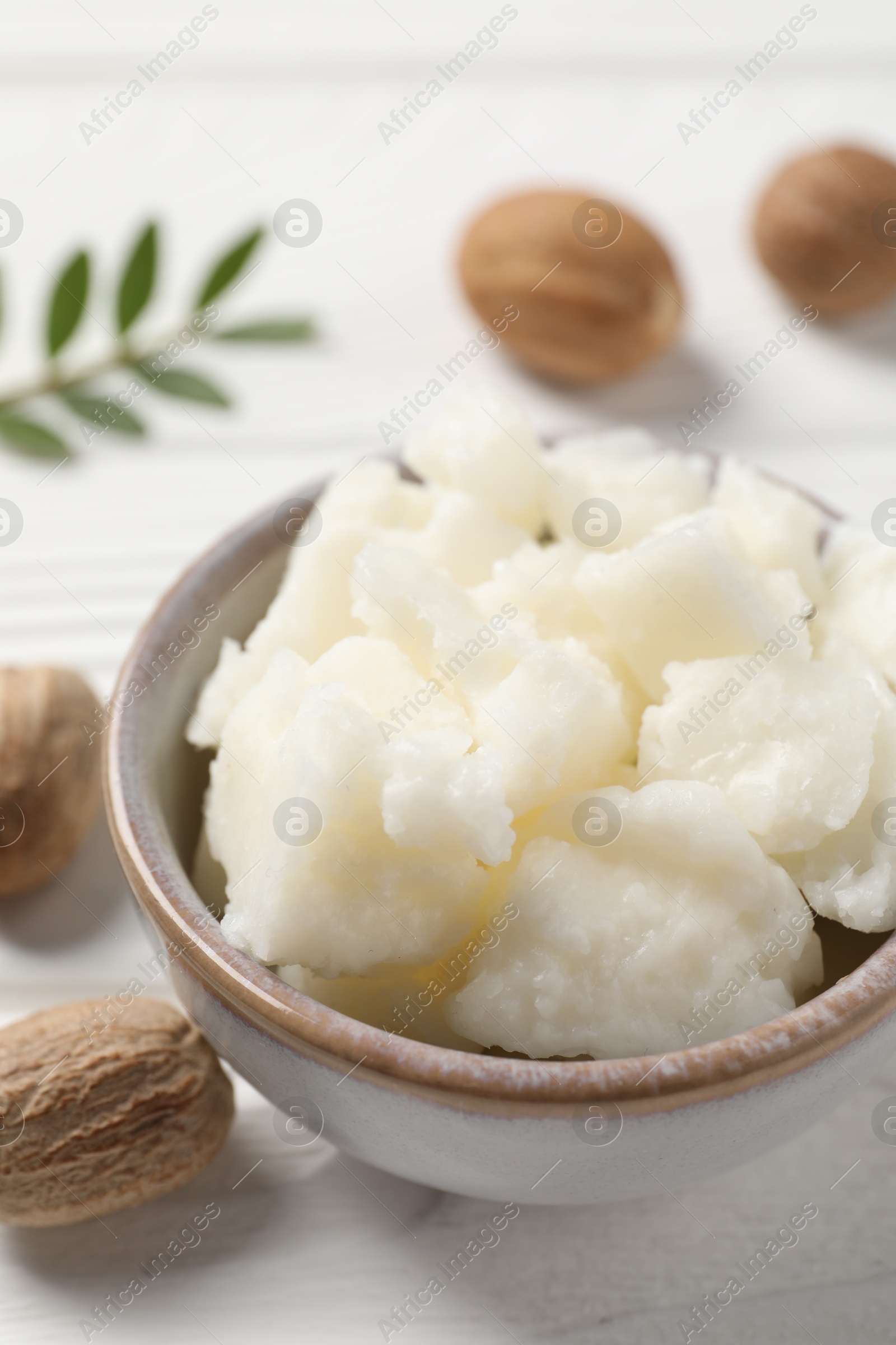 Photo of Shea butter in bowl and nuts on white wooden table, closeup