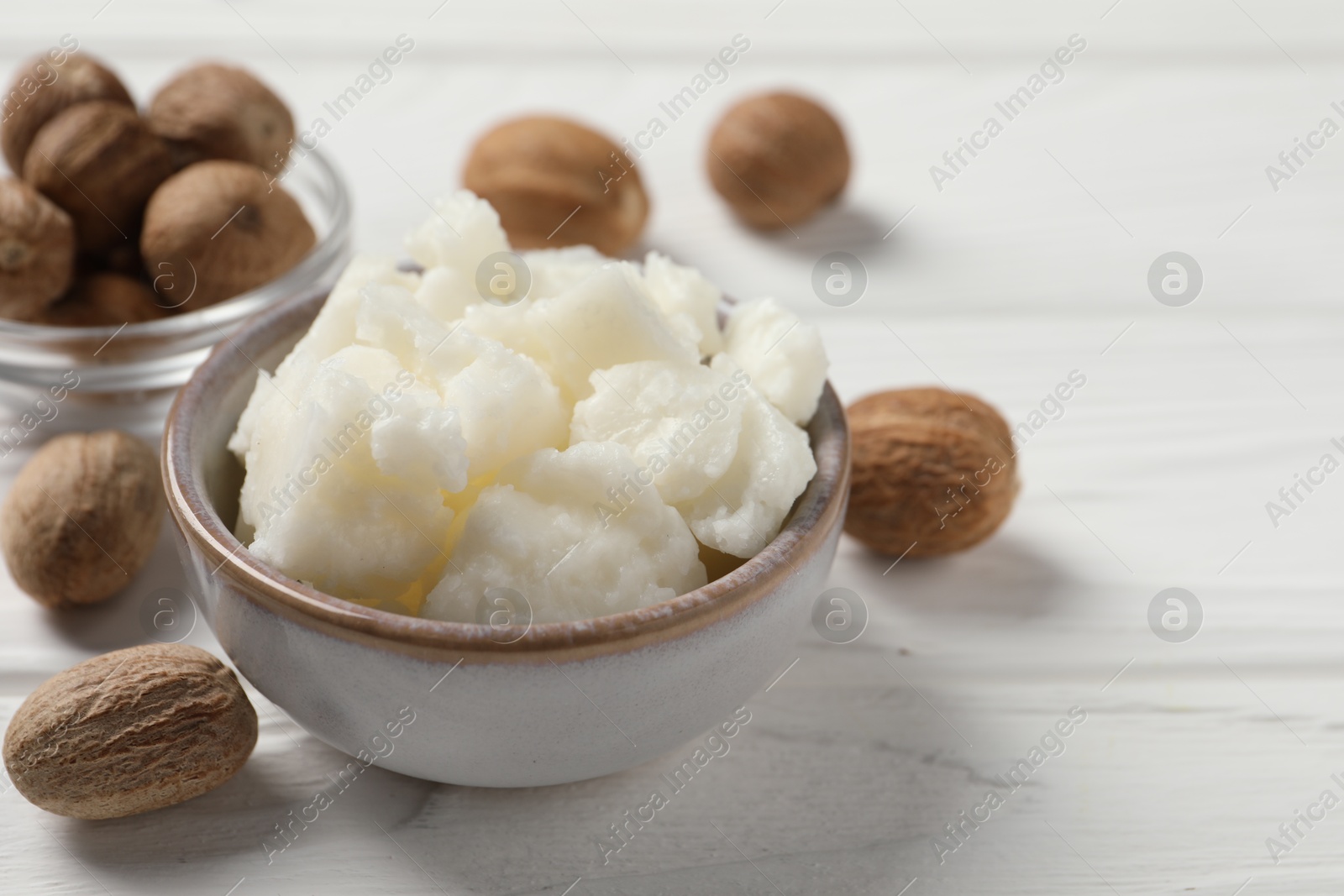 Photo of Shea butter in bowl and nuts on white wooden table, closeup