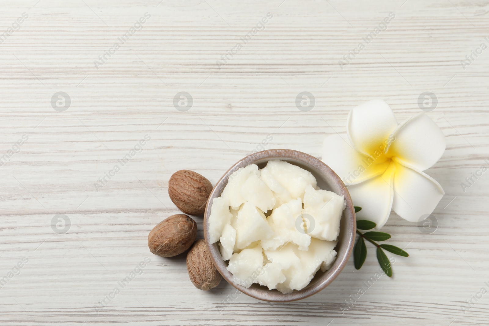 Photo of Shea butter in bowl, flower and nuts on white wooden table, flat lay. Space for text