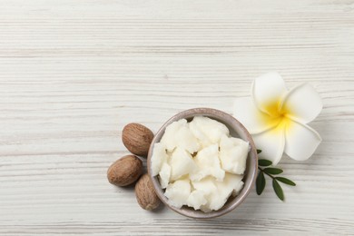 Shea butter in bowl, flower and nuts on white wooden table, flat lay. Space for text