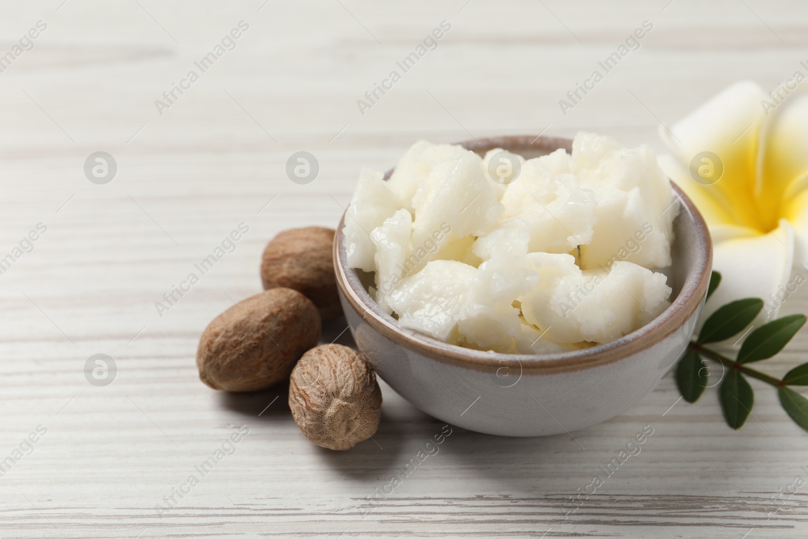 Photo of Shea butter in bowl, flower and nuts on white wooden table, closeup. Space for text