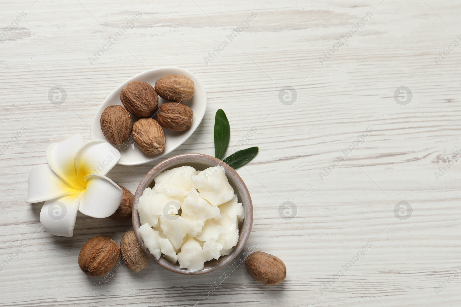 Photo of Shea butter in bowl, flower and nuts on white wooden table, flat lay. Space for text