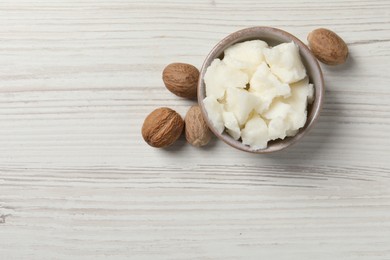 Photo of Shea butter in bowl and nuts on white wooden table, top view. Space for text