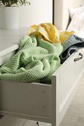 Cluttered chest of drawers indoors, closeup. Clothes in mess