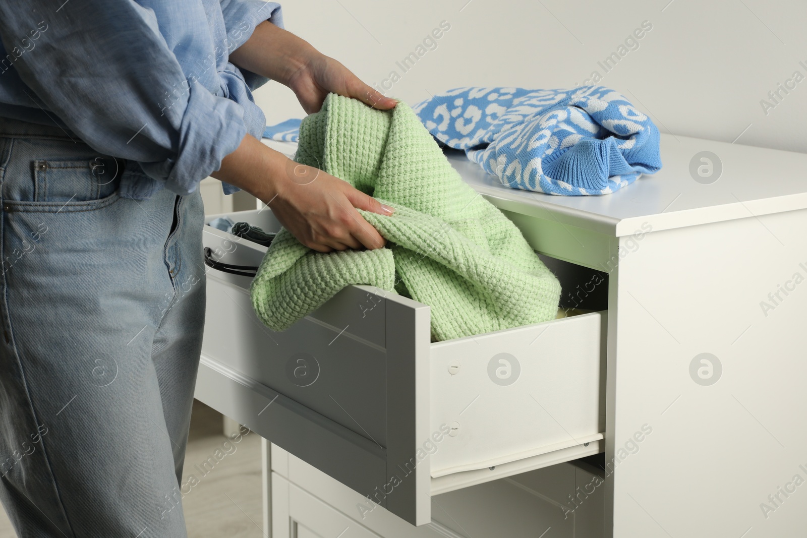 Photo of Woman organizing clothes in chest of drawers indoors, closeup