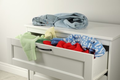 Photo of Cluttered chest of drawers indoors, closeup. Clothes in mess