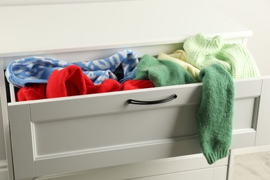 Cluttered chest of drawers indoors, closeup. Clothes in mess