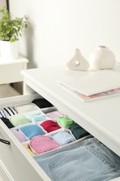 Photo of Chest of drawers with different folded clothes indoors, closeup