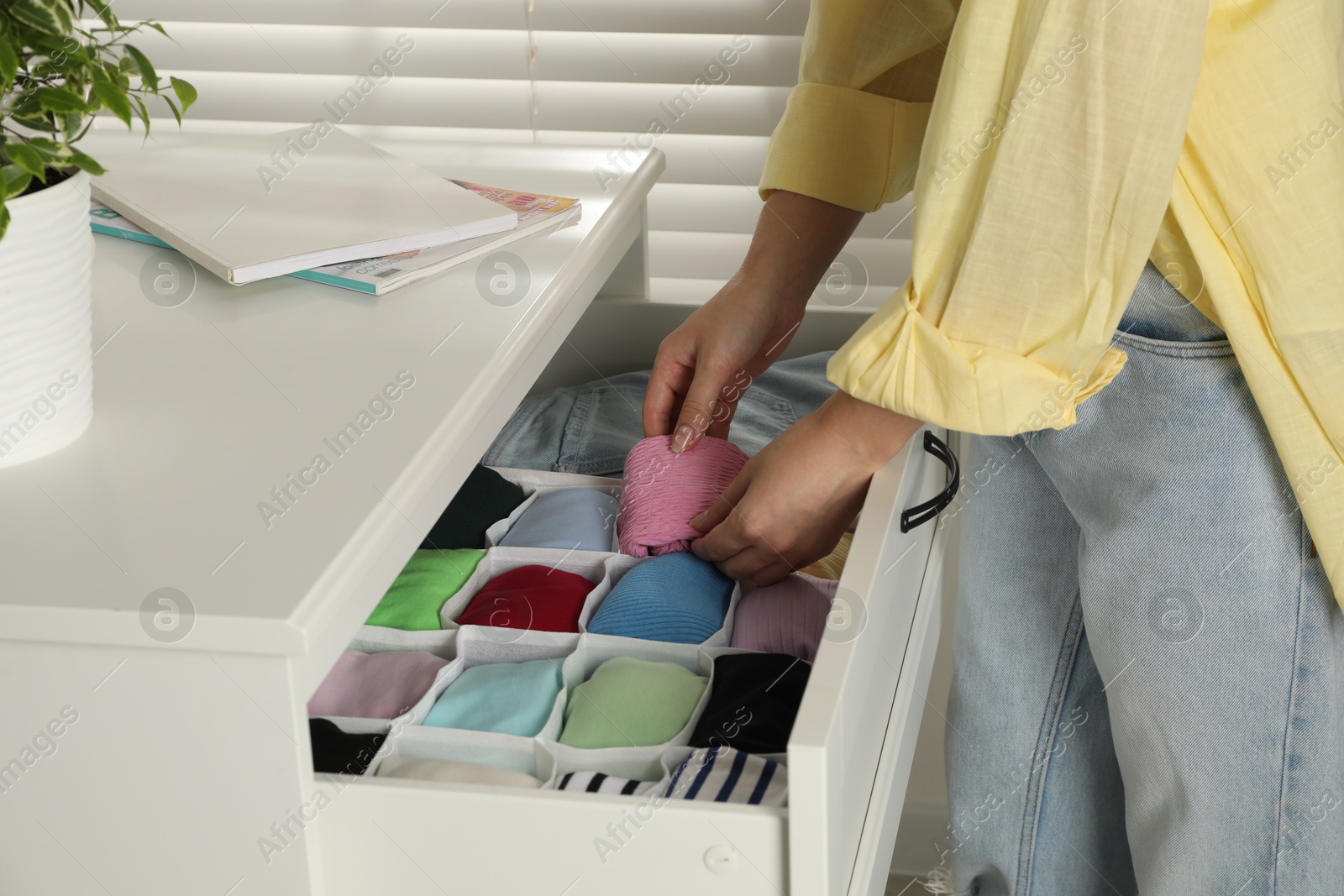 Photo of Woman organizing clothes in chest of drawers indoors, closeup