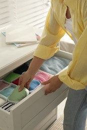 Woman organizing clothes in chest of drawers indoors, closeup