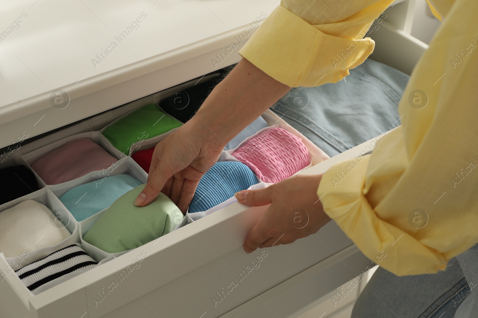 Photo of Woman organizing clothes in chest of drawers indoors, closeup