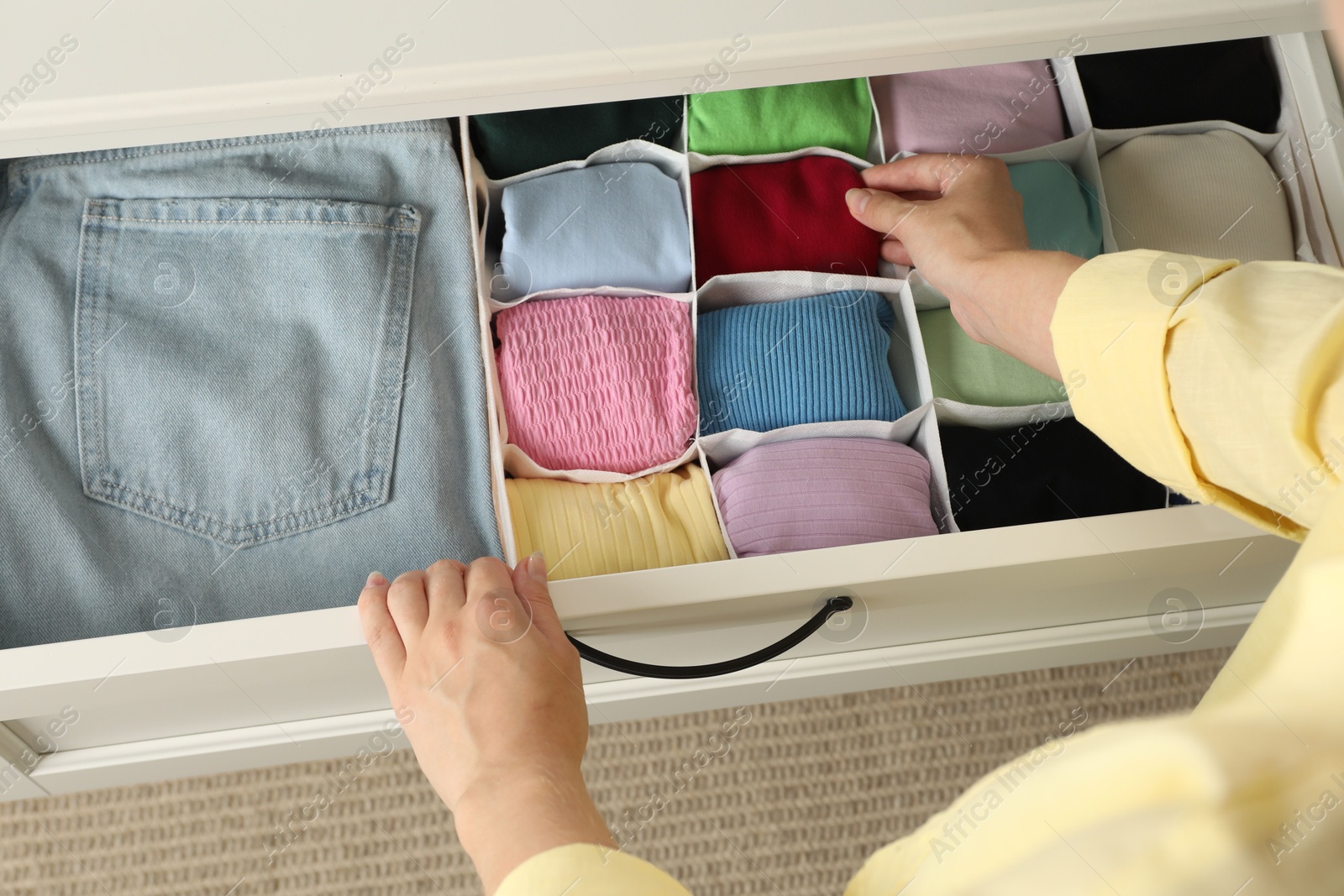 Photo of Woman organizing clothes in chest of drawers indoors, above view