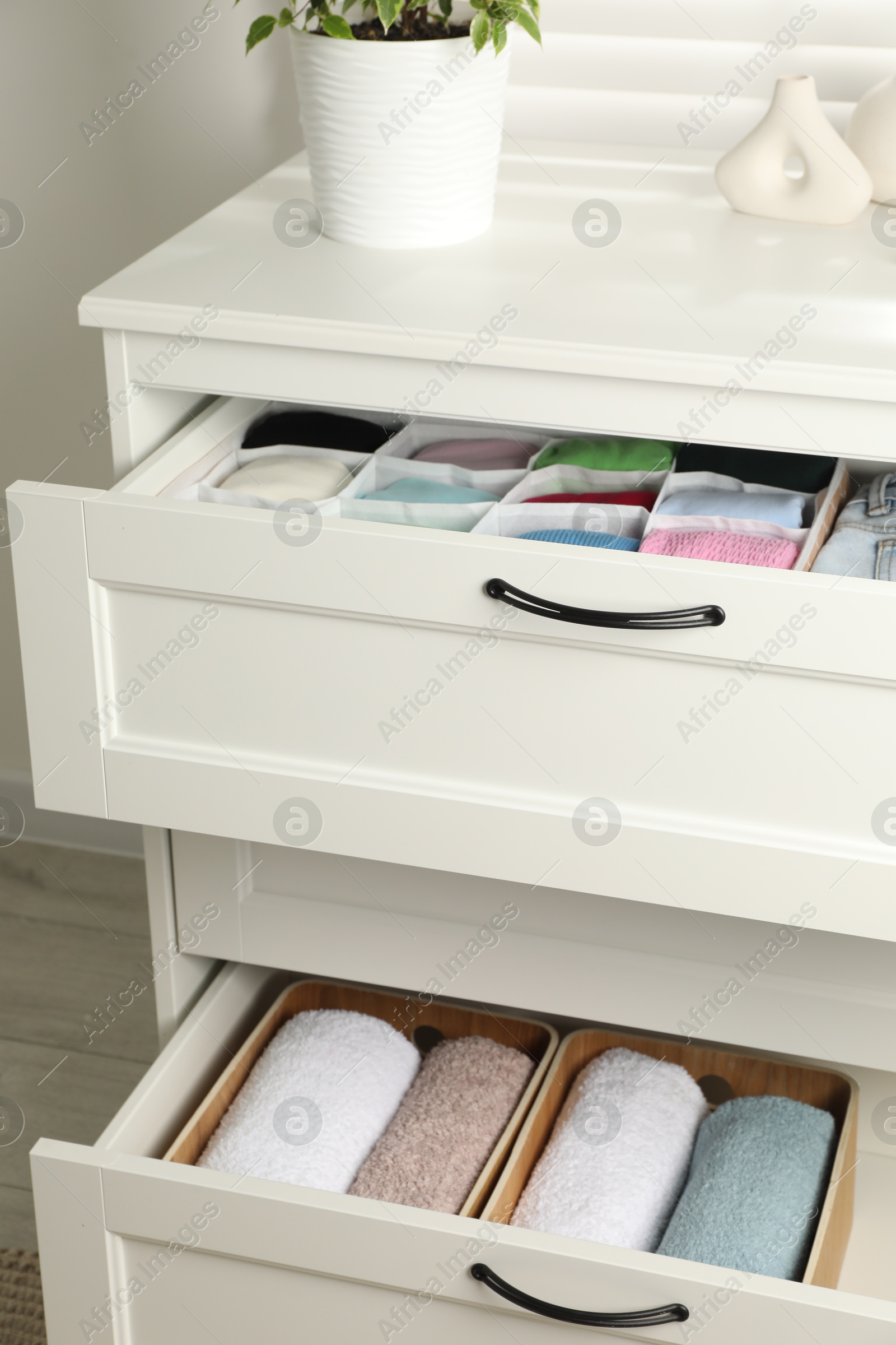 Photo of Chest of drawers with different folded clothes indoors, closeup