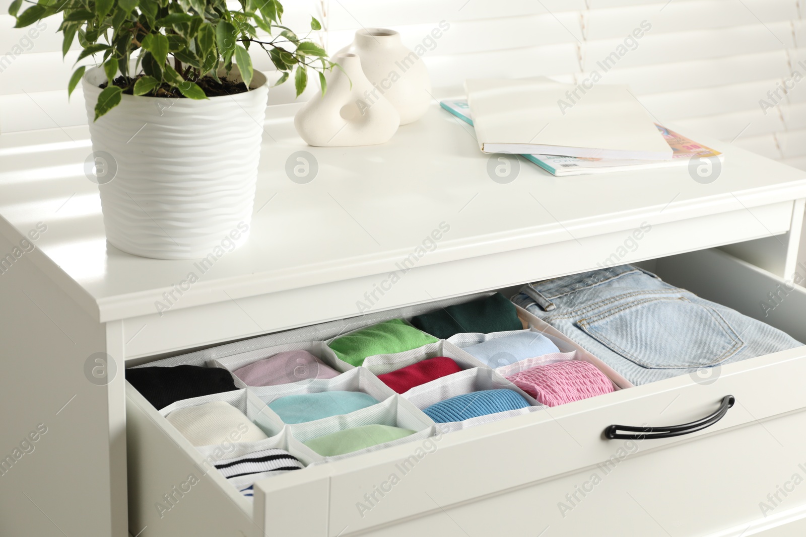 Photo of Chest of drawers with different folded clothes indoors, closeup