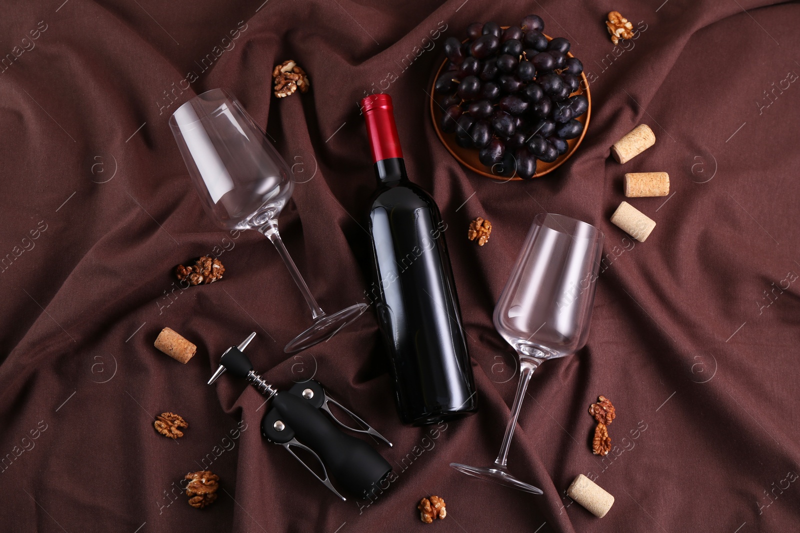 Photo of Flat lay composition with wing corkscrew and wine on brown fabric