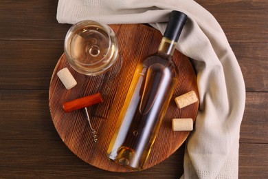 Photo of Corkscrew, glass of wine, bottle and corks on wooden table, top view