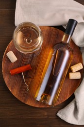 Photo of Corkscrew, glass of wine, bottle and corks on wooden table, top view