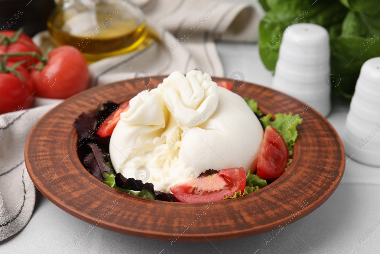 Photo of Delicious burrata salad in bowl on white table, closeup