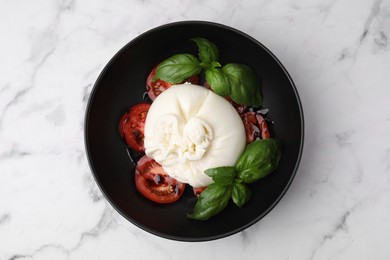 Delicious burrata cheese, tomatoes and basil in bowl on white marble table, top view