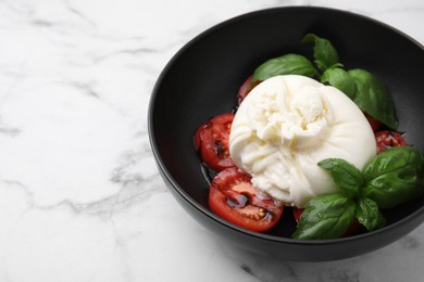 Photo of Delicious burrata cheese, tomatoes and basil in bowl on white marble table, closeup. Space for text