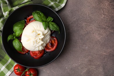 Photo of Delicious burrata cheese, tomatoes and basil in bowl on brown table, top view. Space for text