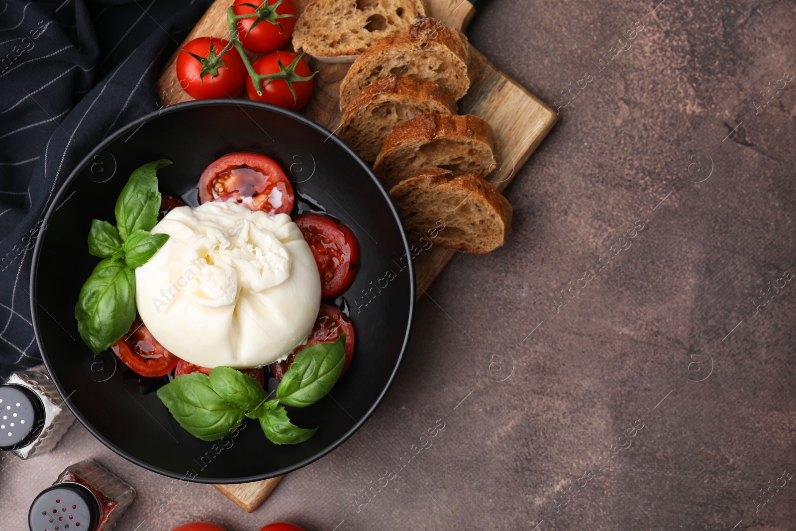 Photo of Delicious burrata cheese, tomatoes, basil and bread in bowl on brown table, flat lay. Space for text