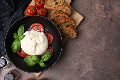 Delicious burrata cheese, tomatoes, basil and bread in bowl on brown table, flat lay. Space for text