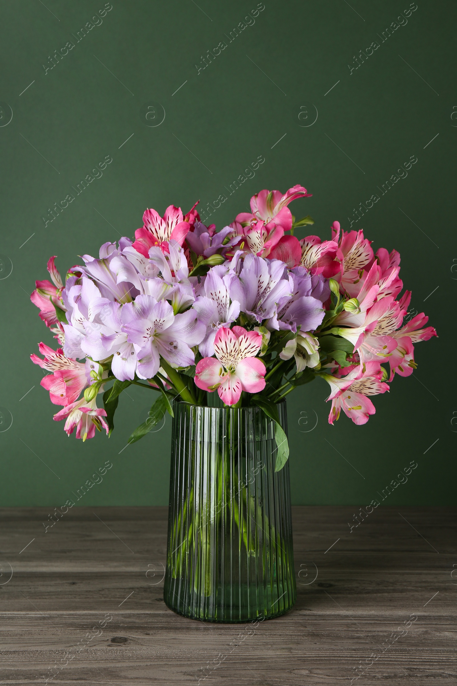 Photo of Beautiful alstroemeria flowers in vase on wooden table against green background