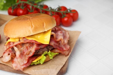 Delicious burger with bacon, patty and cheese on white tiled table, space for text