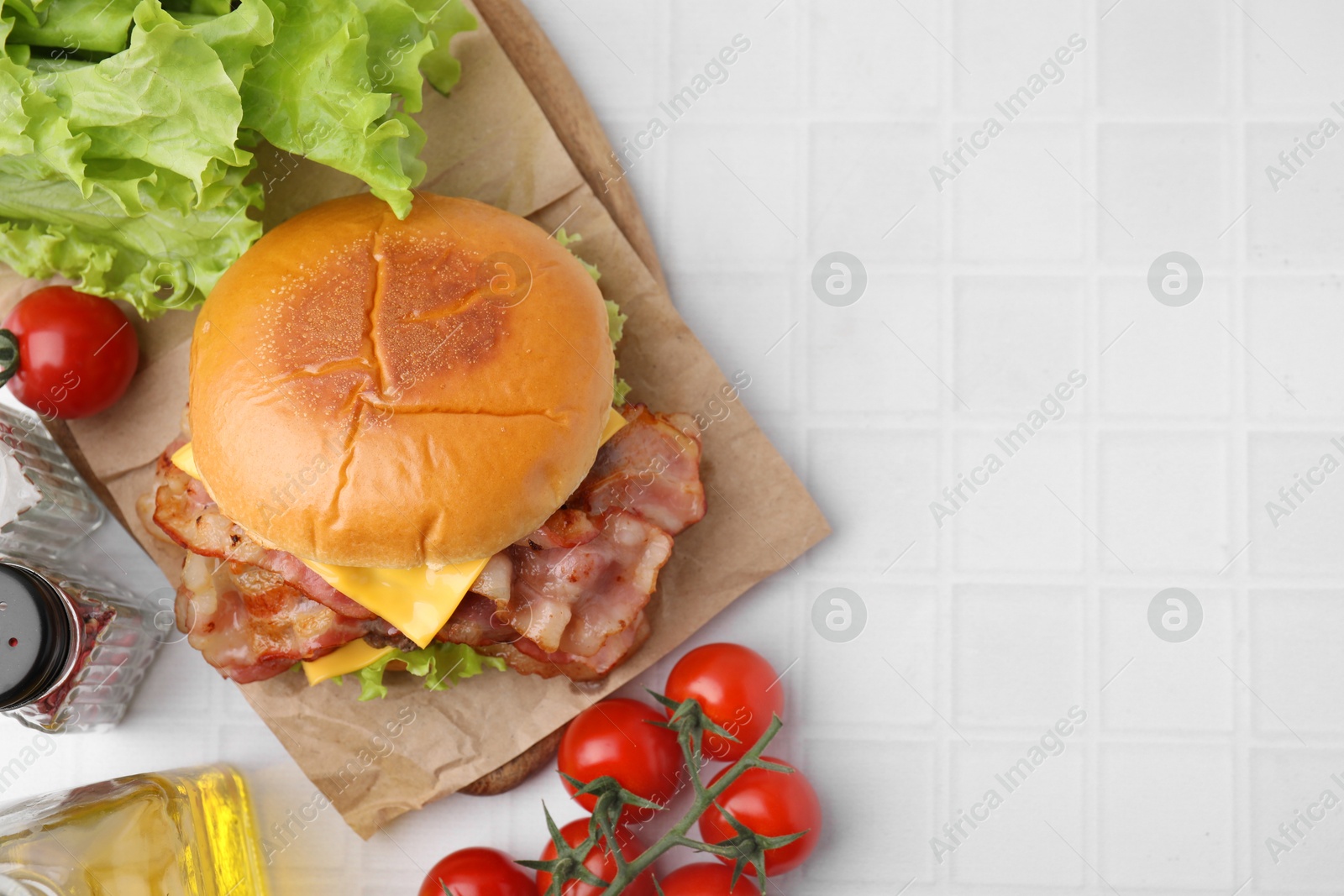 Photo of Delicious burger with bacon served on white tiled table, top view. Space for text