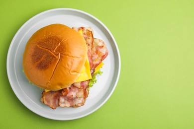 Photo of Delicious burger with bacon and cheese on green background, top view. Space for text