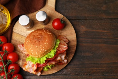 Photo of Delicious burger with bacon, tomatoes and lettuce on wooden table, top view. Space for text