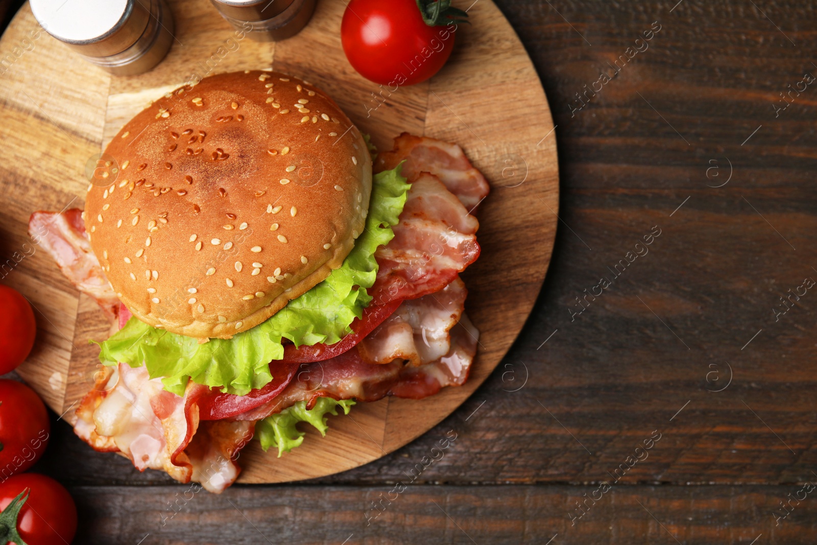 Photo of Delicious burger with bacon, tomatoes and lettuce on wooden table, top view. Space for text