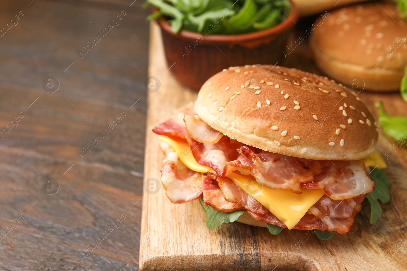 Photo of Delicious burger with bacon and cheese on wooden table, space for text