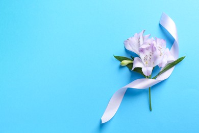 Photo of Beautiful alstroemeria flowers and ribbon on light blue background, top view. Space for text