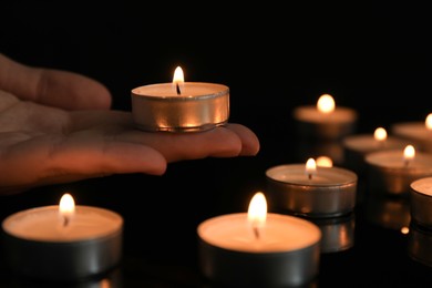 Photo of Woman holding burning tealight candle on black background, closeup