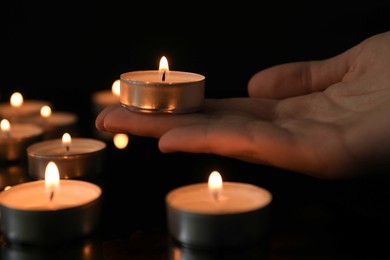 Photo of Woman holding burning tealight candle on black background, closeup