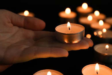 Woman holding burning tealight candle on black background, closeup