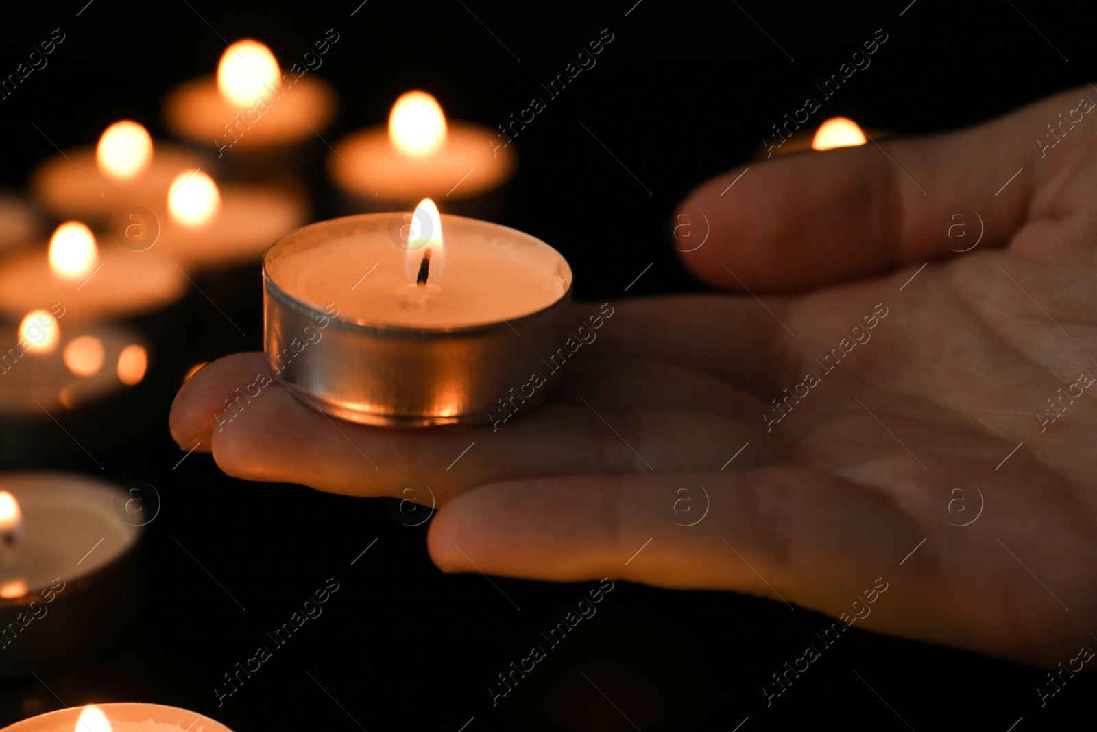 Photo of Woman holding burning tealight candle on black background, closeup