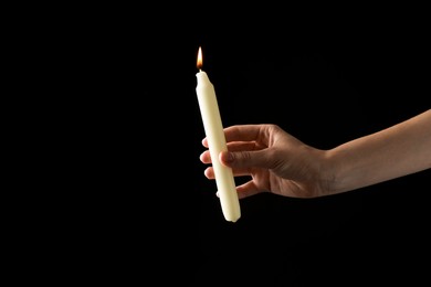 Photo of Woman holding burning candle on black background, closeup. Space for text