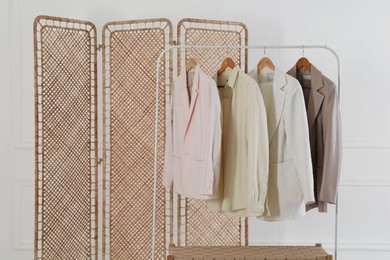 Photo of Folding screen, rack with clothes and storage bench near white wall indoors