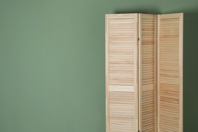 Photo of Wooden folding screen near green wall indoors, space for text