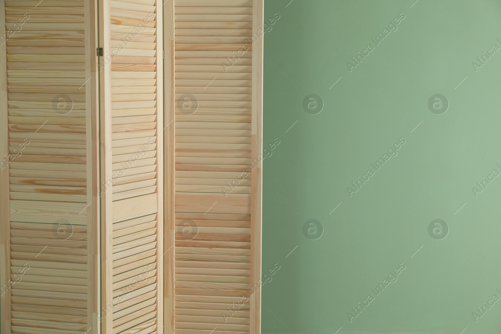 Photo of Wooden folding screen near green wall indoors, space for text