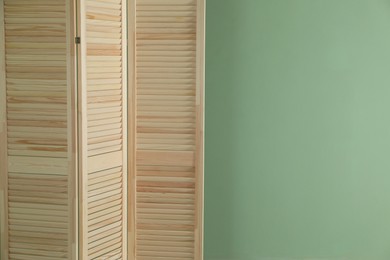 Photo of Wooden folding screen near green wall indoors, space for text