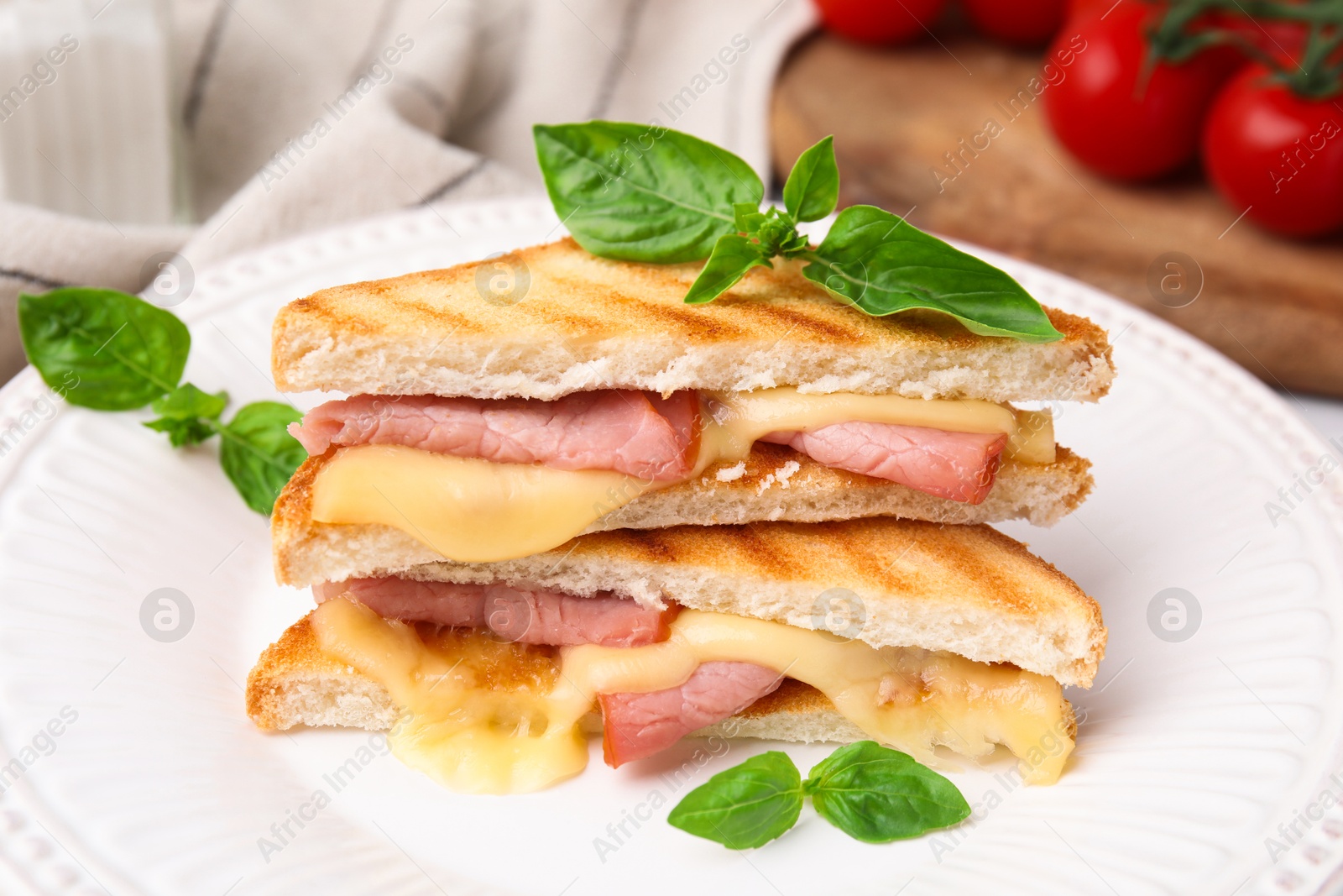 Photo of Pieces of toasted bread with melted cheese, ham and basil on table