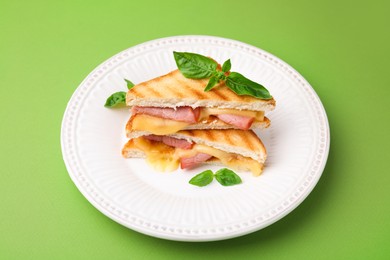 Pieces of toasted bread with melted cheese, ham and basil on green background