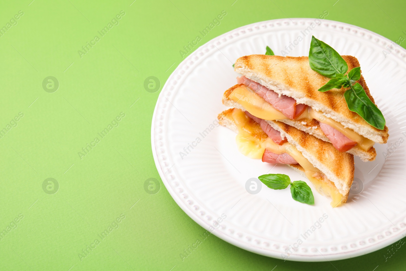 Photo of Pieces of toasted bread with melted cheese, ham and basil on green background, space for text