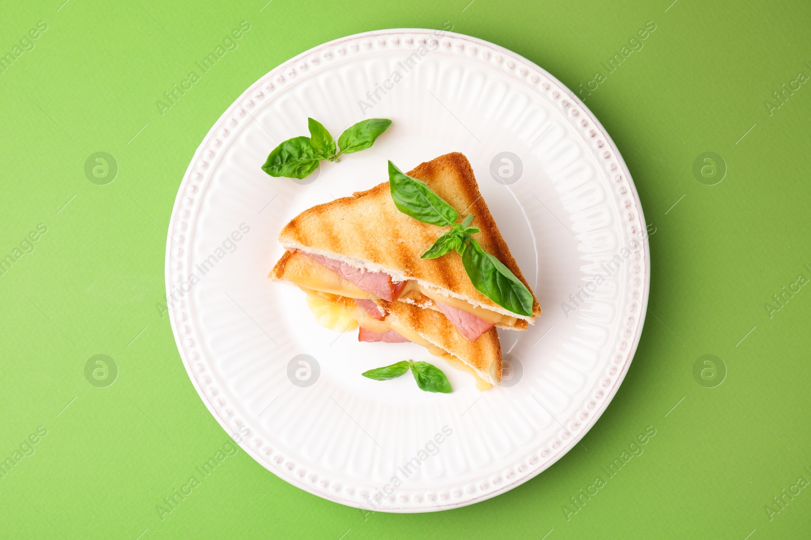 Photo of Pieces of toasted bread with melted cheese, ham and basil on green background, top view