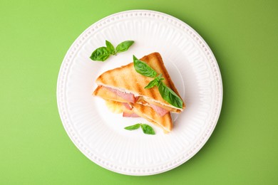 Pieces of toasted bread with melted cheese, ham and basil on green background, top view